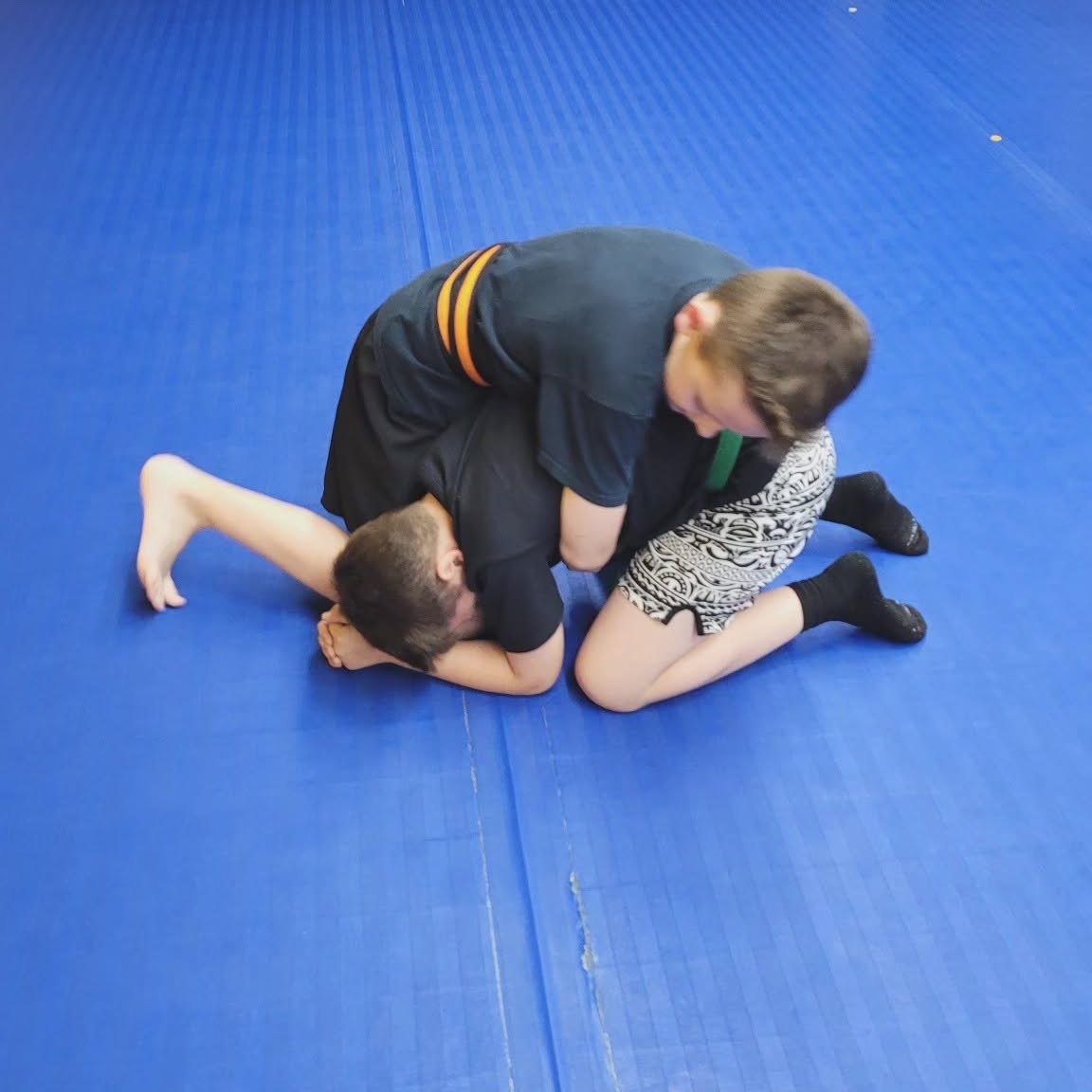 Two adult students drilling a ground control position on the blue mats at Makoto Jiu Jitsu Centers in Deer Park